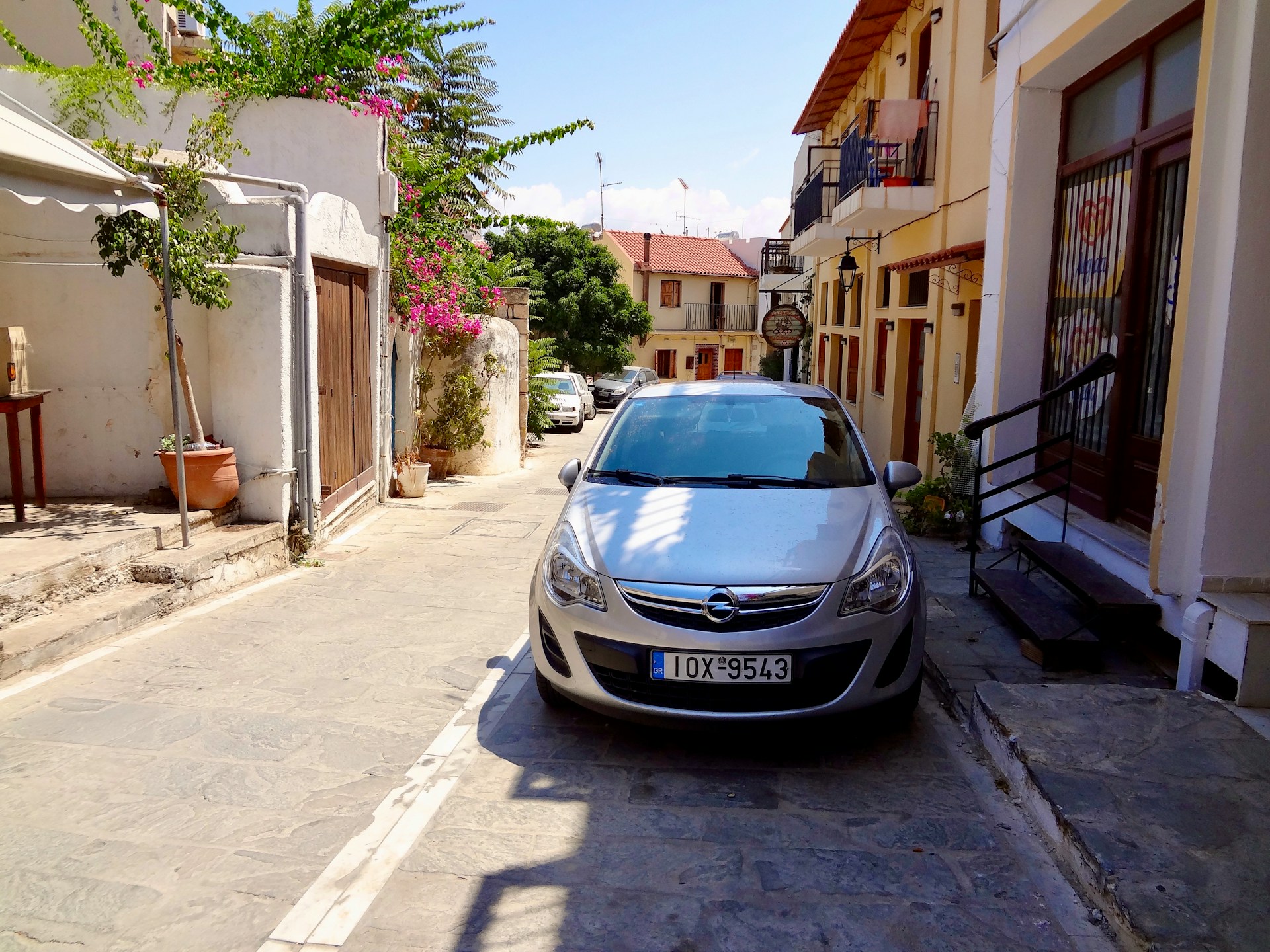 a grey car parked in front of a concrete building in a small town in Greece