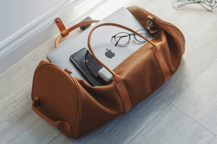 silver Macbook and smartphone in a brown duffel bag silver Macbook and smartphone in a brown duffel bag