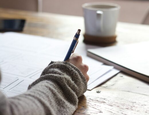 person writing on papers with a ceramic coffee mug on wooden table