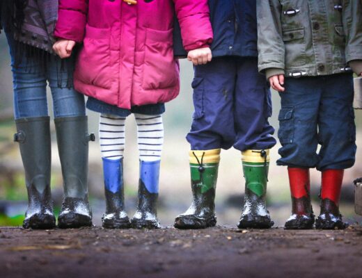 four children standing on mud with rain boots