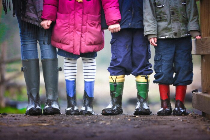 four children standing on mud with rain boots