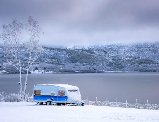 white and blue caravan parked on the snow in front of water in Tromso, Norway
