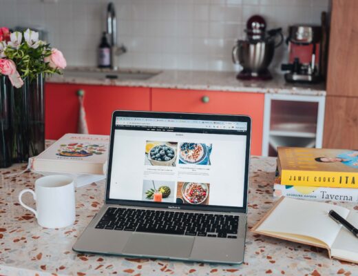 Laptop on a marble kitchen counter with a coffee cup, flowers and cookbooks