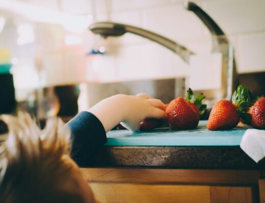 A toddler pulling hand up to the kitchen counter to grab a strawberry