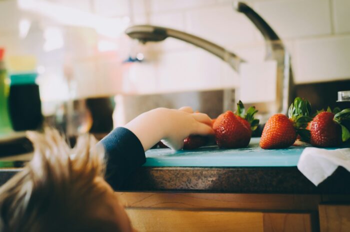 A toddler pulling hand up to the kitchen counter to grab a strawberry