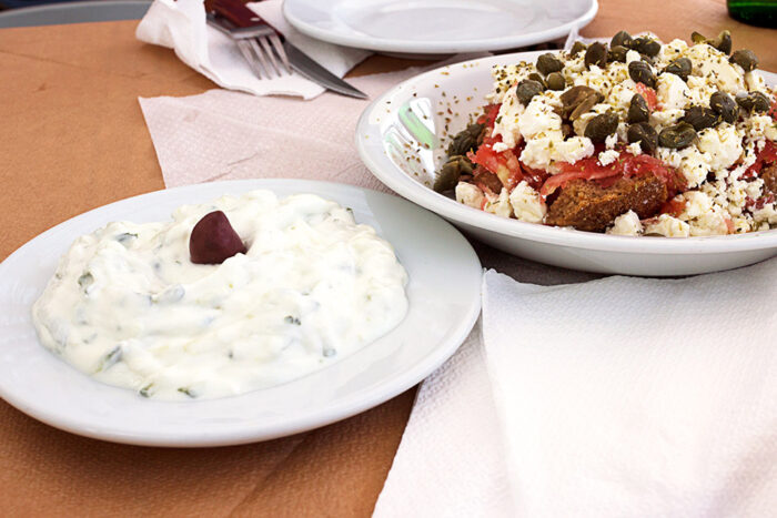 A bowl of Greek tzaziki and a Greek salad on a table