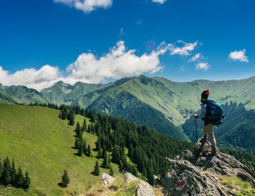 A man hiking and standing on a rock looking at mountains in Romania