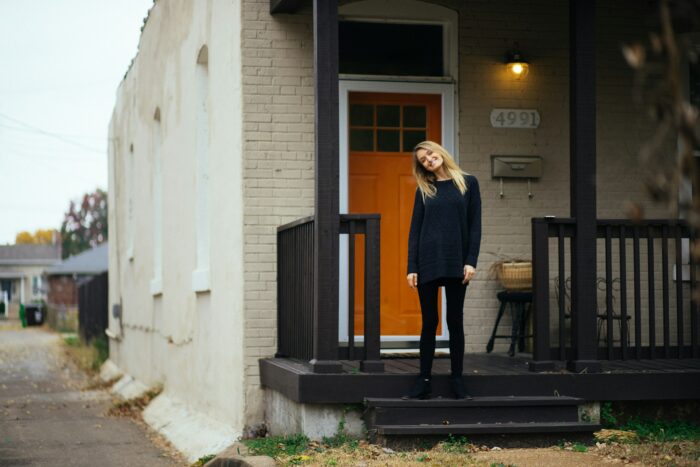 a blonde woman standing on a porch in front of a house