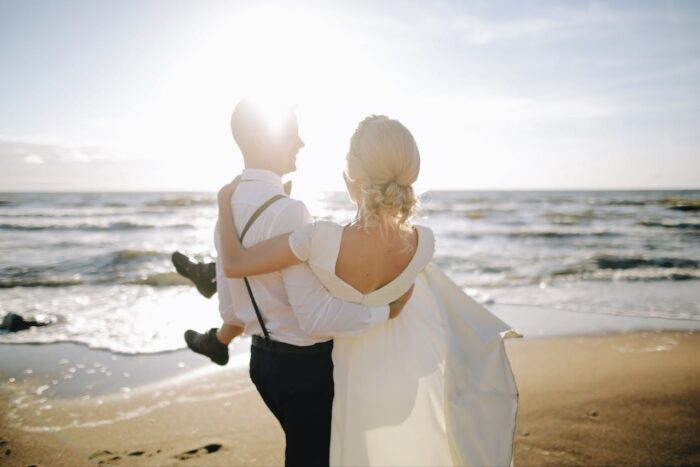 man lifting woman in wedding dress on the beach