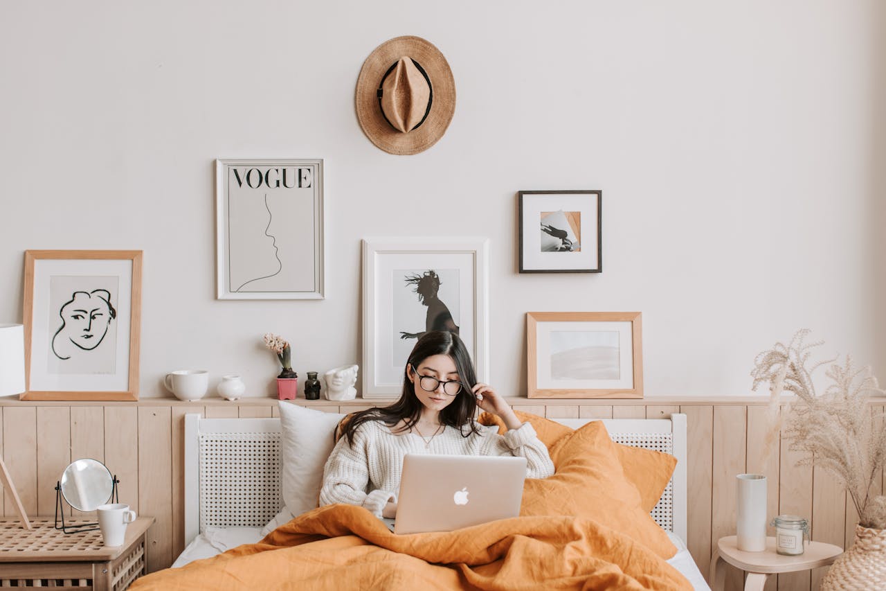 woman using laptop in bed in front of white wall with prints