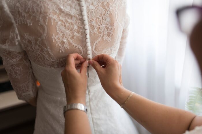 woman tying buttons on a wedding dress with white lace