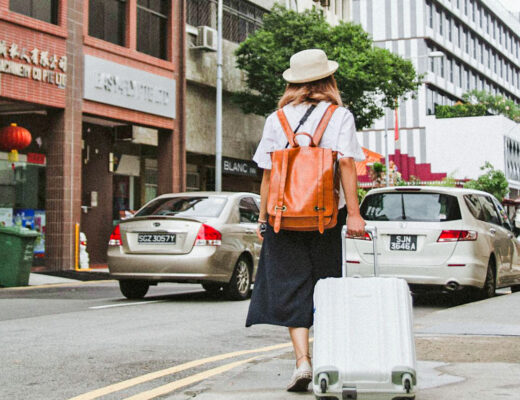 woman walking on the street in asia carrying a suitcase and wearing a white hat