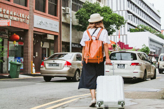woman walking on the street in asia carrying a suitcase and wearing a white hat