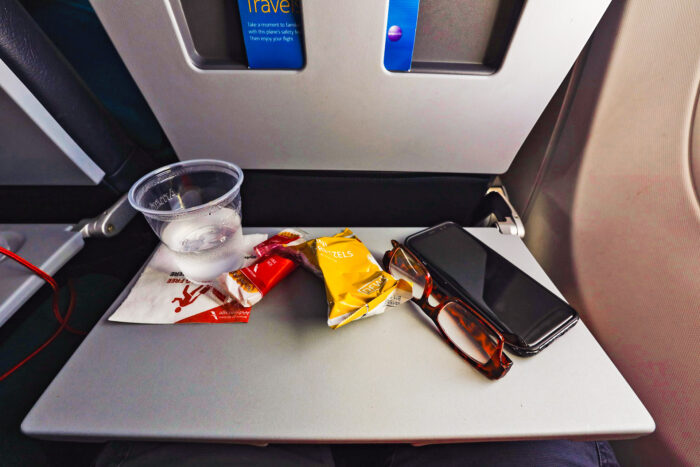 an airplane tray with snacks and a plastic glass of water and a smartphone