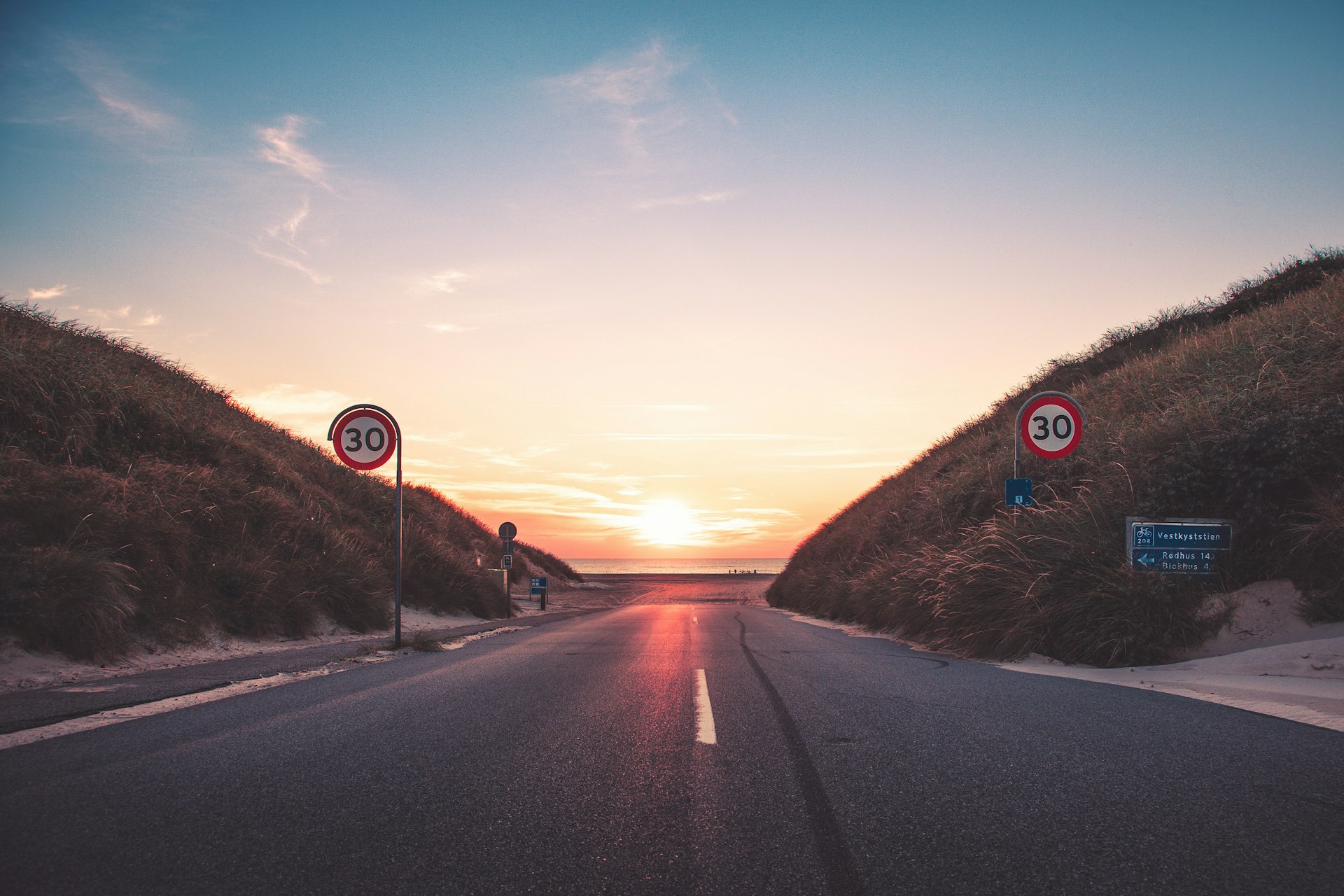 grey asphalt, road in Denmark going into the sea at sunset