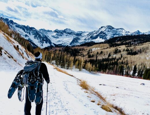 man wearing backpack climbing mountain with snow