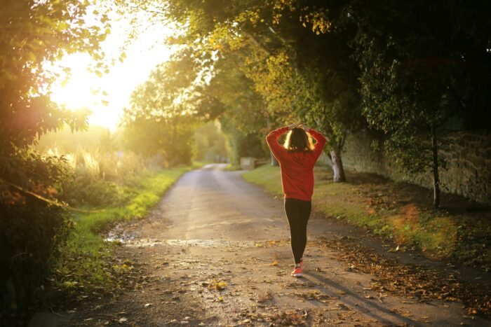 Wellbeing woman in sport clothing walking on a path in a park with sunlight