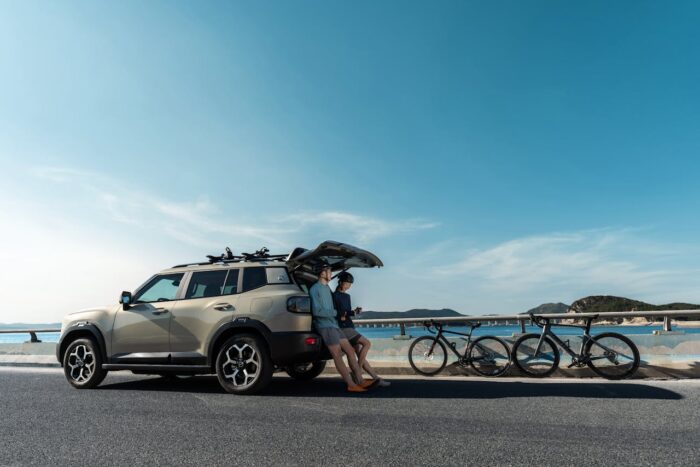 Grey SUV vehicle parked on a coastal road with father and son and bicycles