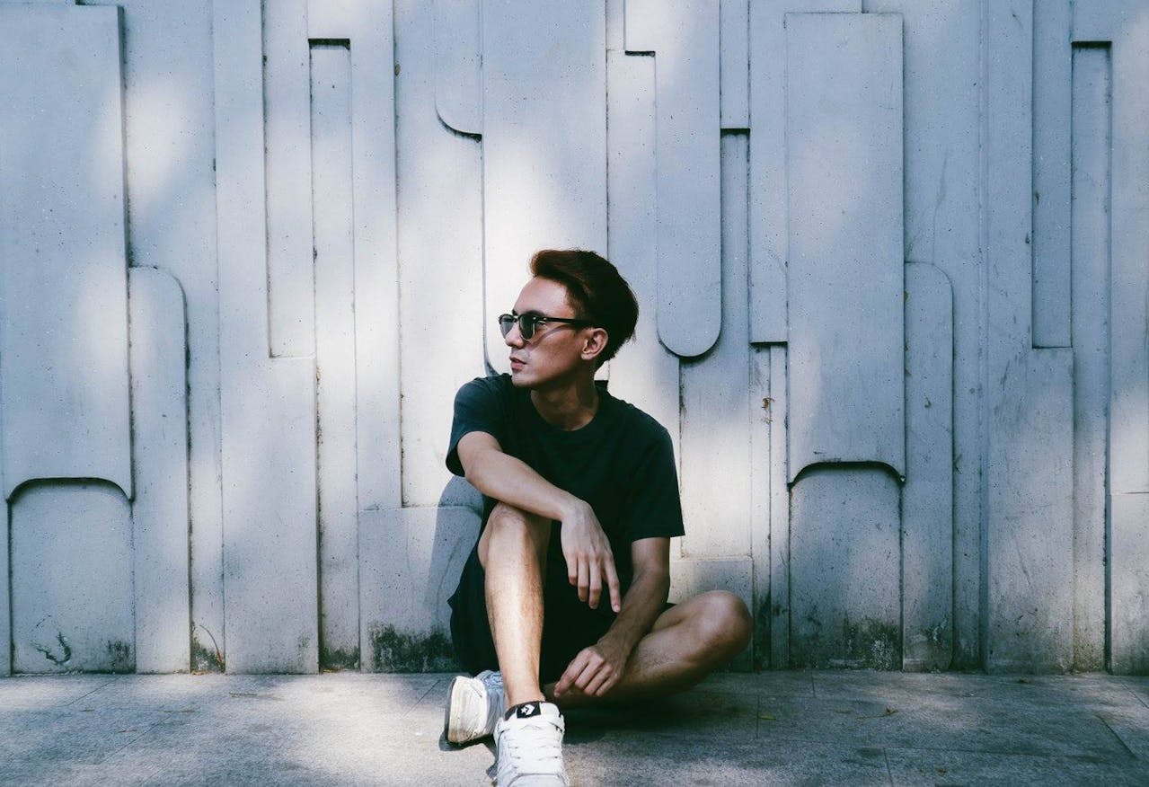 man sitting beside wall wearing ray ban sunglasses