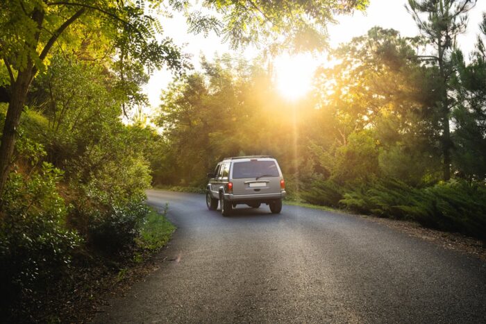 gray SUV car driving on a mountain road with trees and sunset