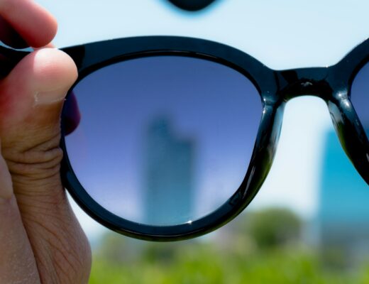 hand holding black frame sunglasses over city landscape