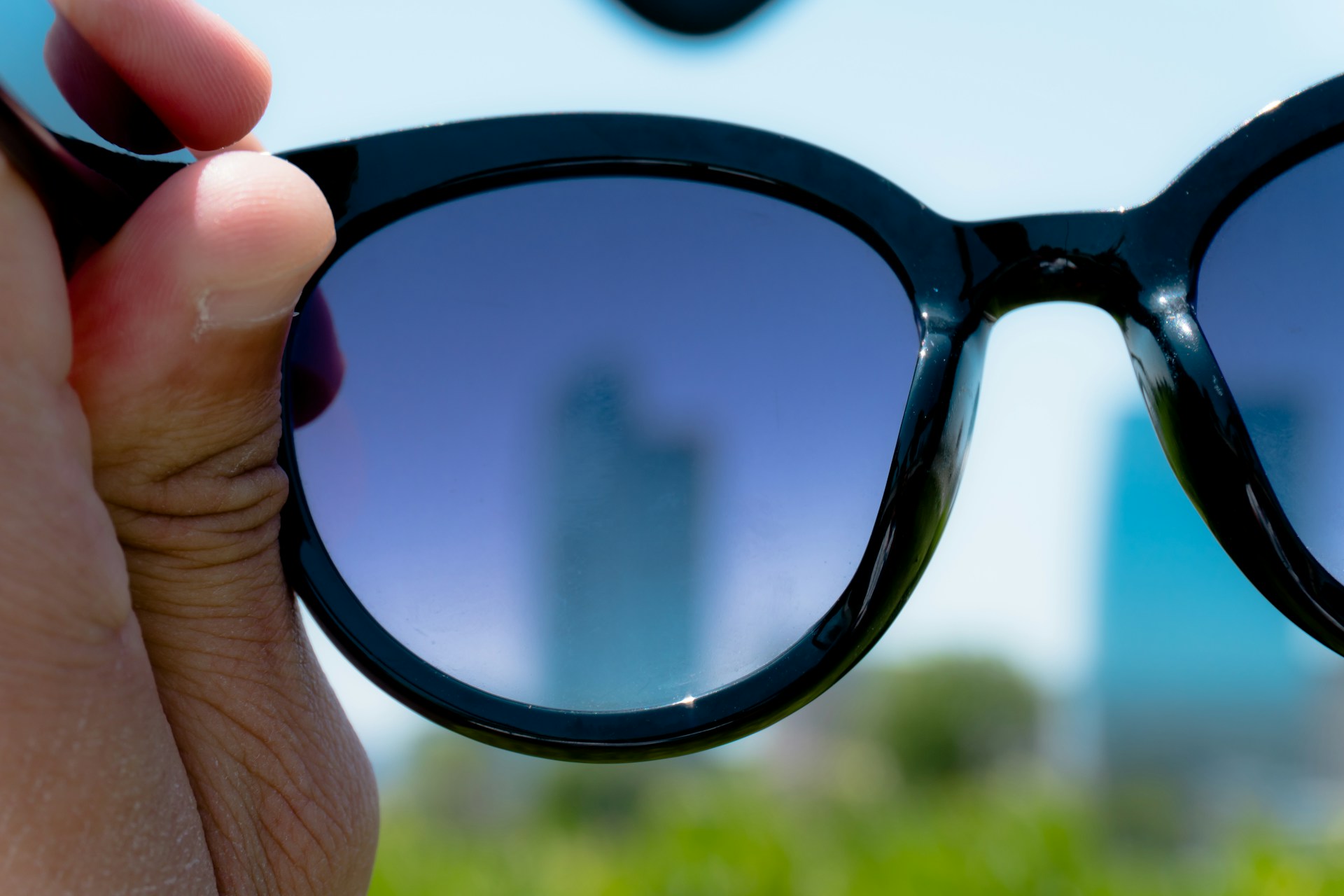 hand holding black frame sunglasses over city landscape