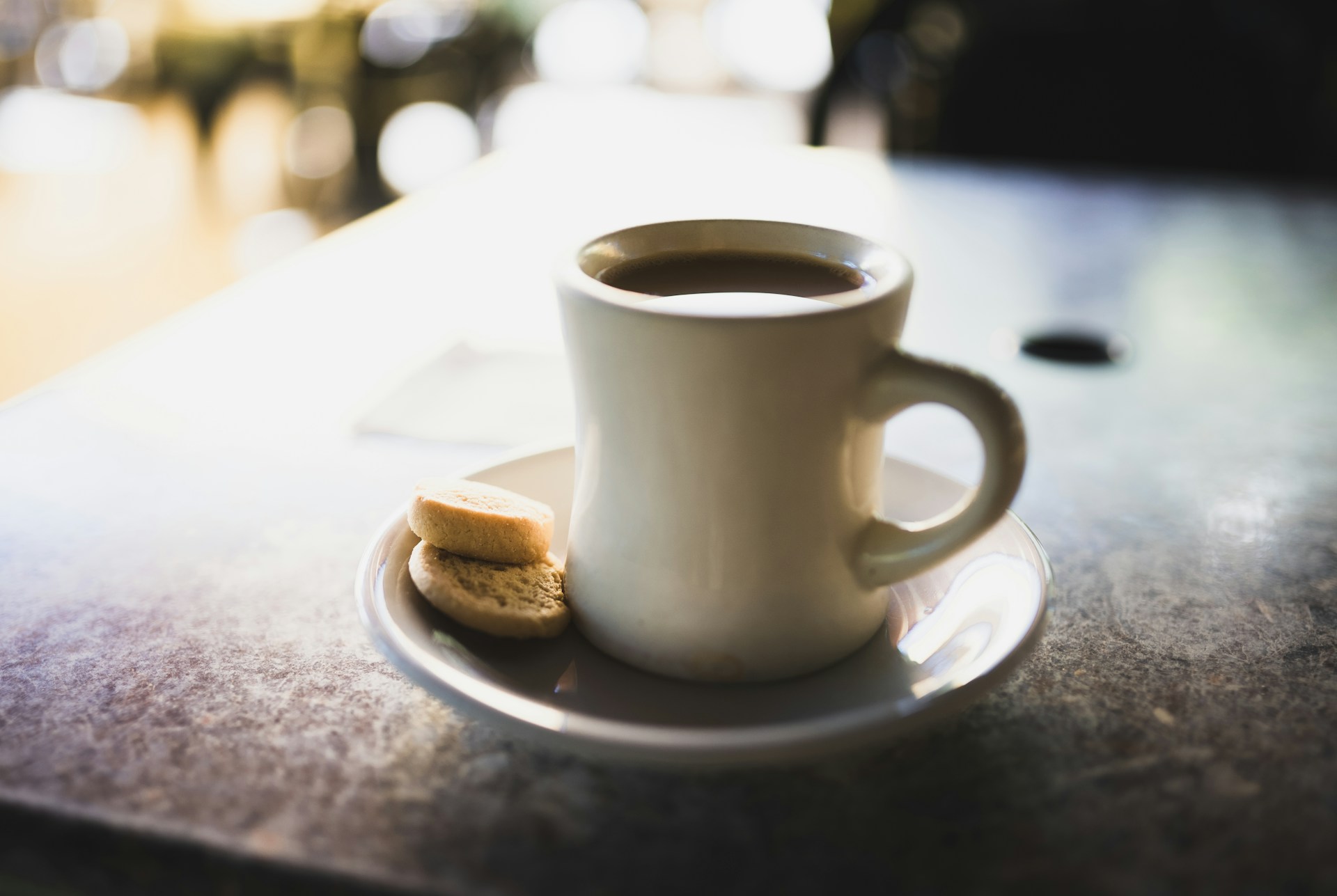 a white cup of black coffee and biscuits on a table a white cup of black coffee and biscuits on a table