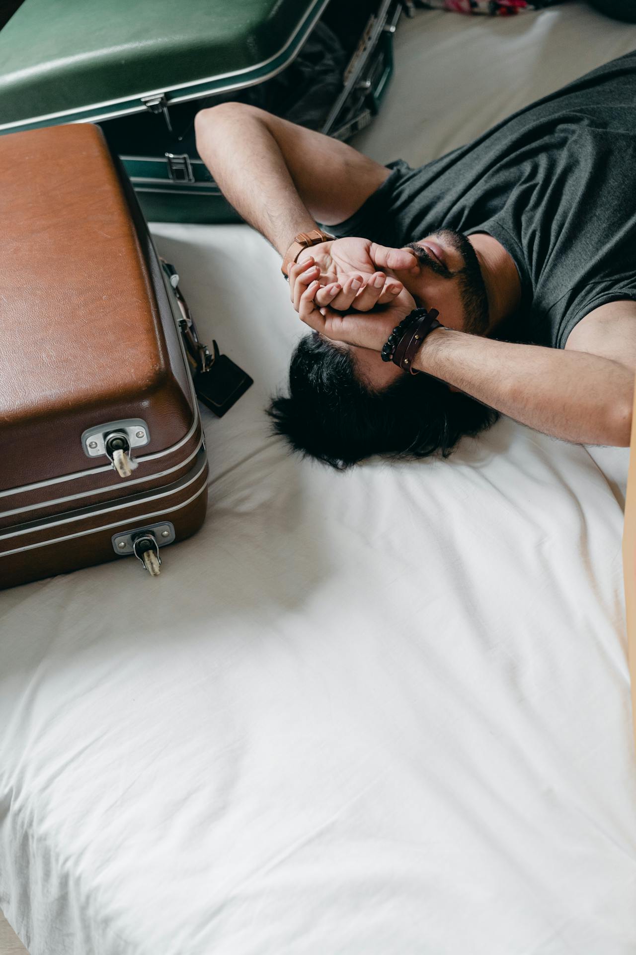 tired man lying on white bed with suitcases