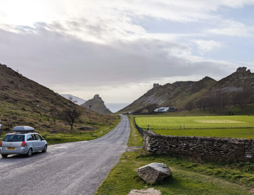 a grey car drives down a rural road towards hills in England