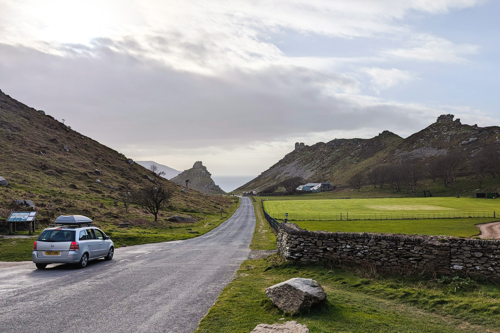 a grey car drives down a rural road towards hills in England