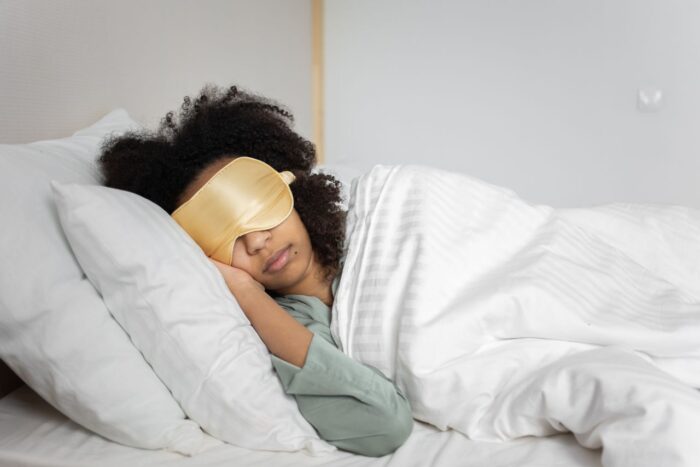 A woman peacefully sleeping with an eye mask in a cozy white bedroom setting. A woman peacefully sleeping with an eye mask in a cozy white bedroom setting.