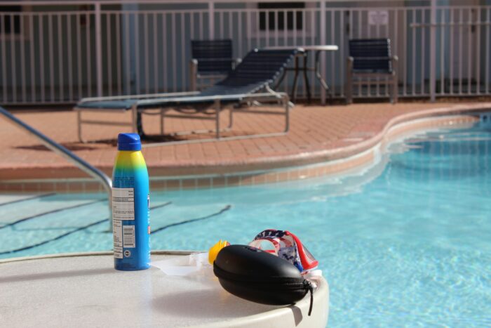 a bottle of sunscreen and swimming goggles in the sunshine next to a swimming pool