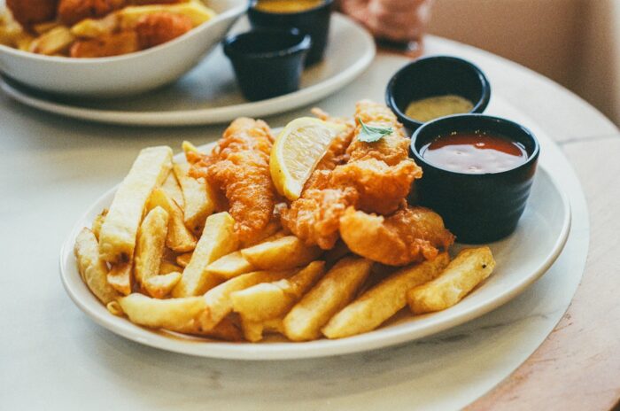 a white plate topped with fried fish, chips and dipping sauce a white plate topped with fried fish, chips and dipping sauce