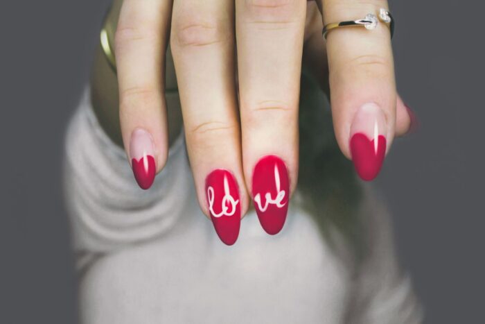 Vibrant red nails with 'love' art on a woman's hand, showcasing elegant style and design. Vibrant red nails with 'love' art on a woman's hand, showcasing elegant style and design.