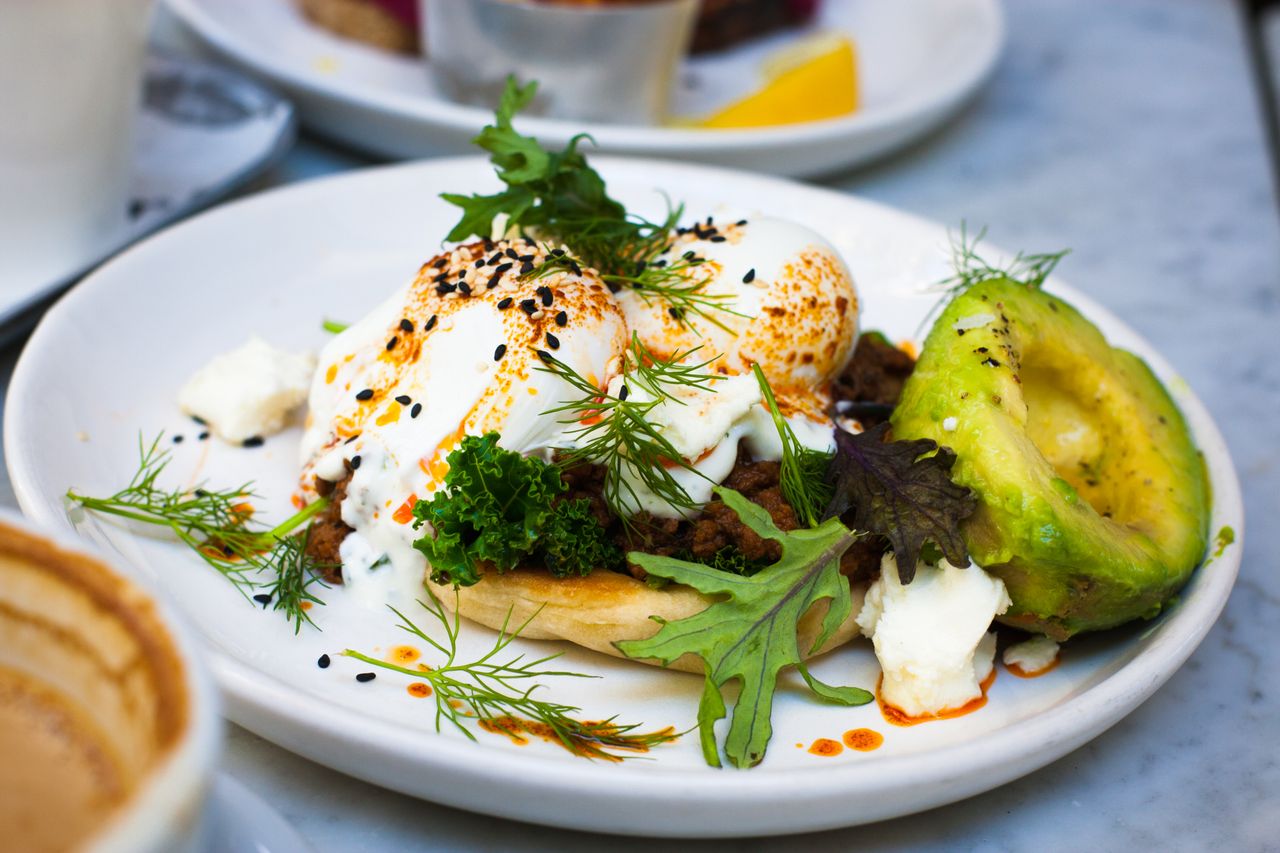 Delicious brunch featuring poached eggs, avocado, and herbs on a plate.