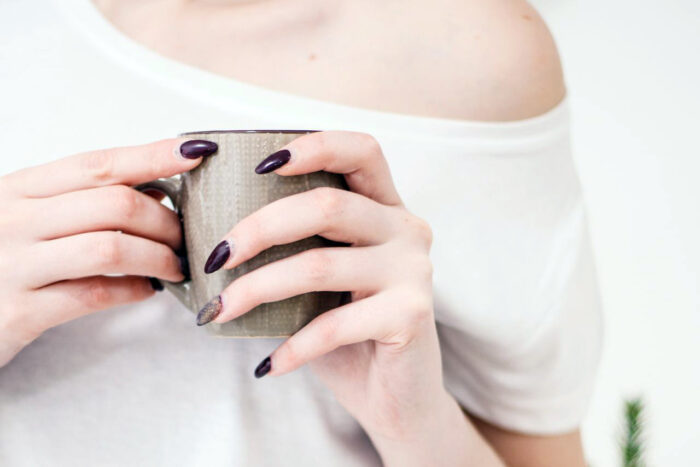 Close-up of a woman with manicured nails holding a mug in a bright, minimalist setting. Close-up of a woman with manicured nails holding a mug in a bright, minimalist setting.