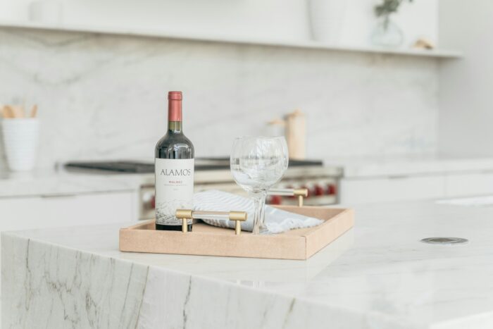 a bottle of red wine on top of a wooden tray on a marble kitchen counter top a bottle of red wine on top of a wooden tray on a marble kitchen counter top