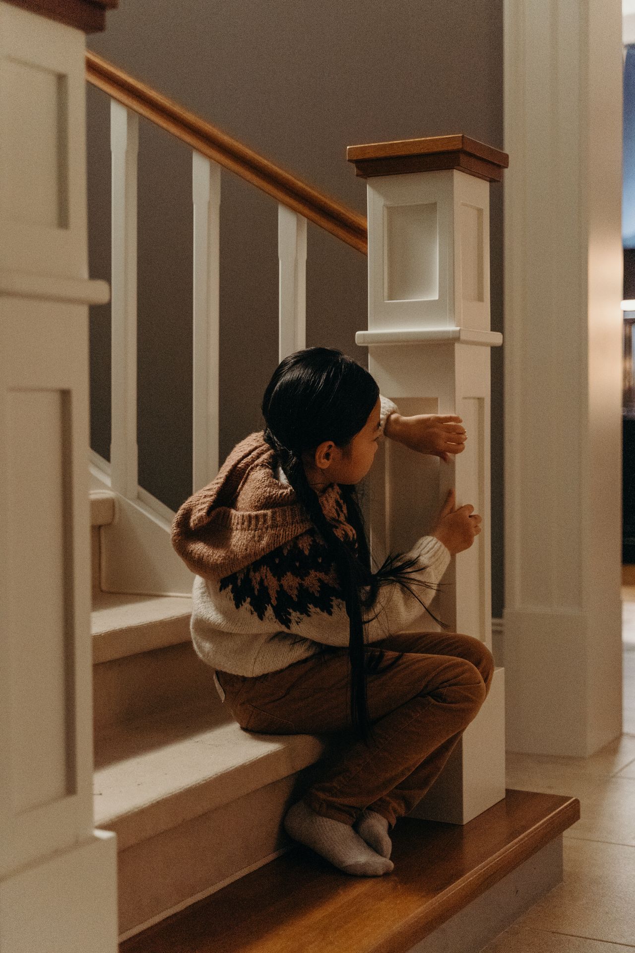 A child sits on stairs indoors, wearing a cozy sweater in a warm home setting. A child sits on stairs indoors, wearing a cozy sweater in a warm home setting.