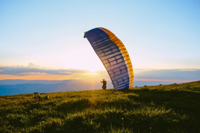 silhouette of person paragliding over hills at sunset in France
