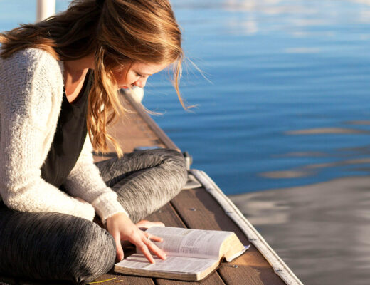 photo of a woman reading a book on a dock near a lake