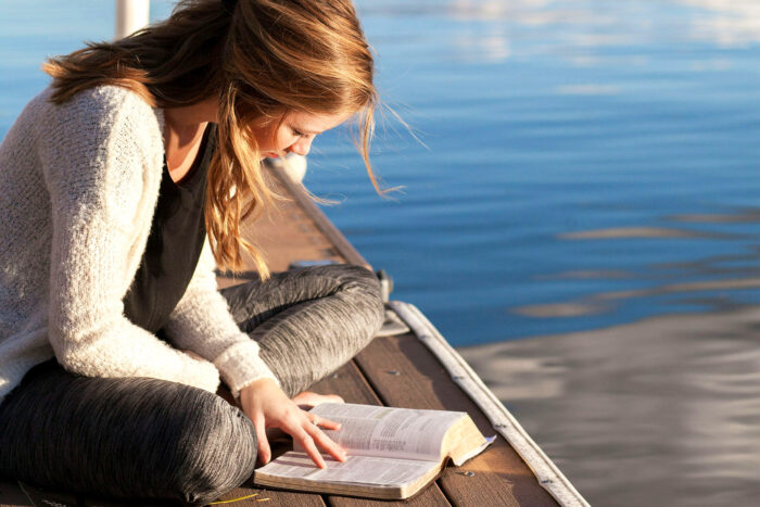 photo of a woman reading a book on a dock near a lake photo of a woman reading a book on a dock near a lake