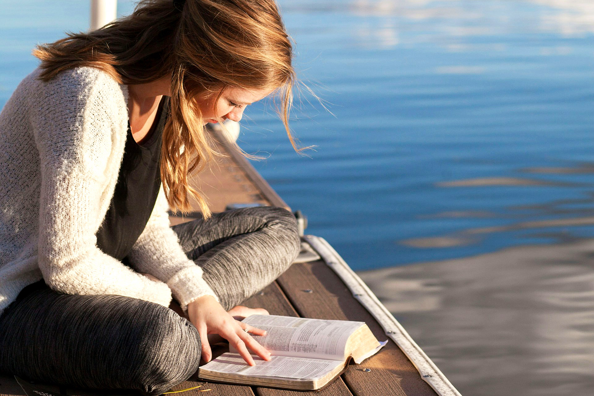 photo of a woman reading a book on a dock near a lake