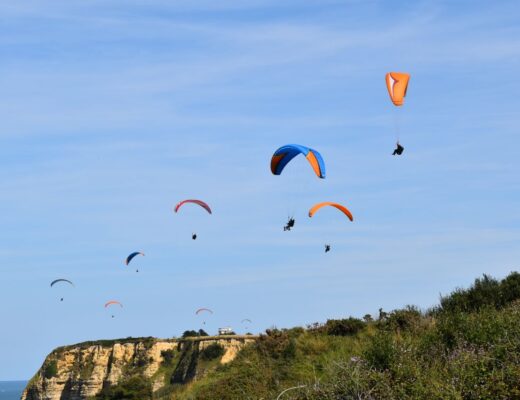 A group of paragliders soar over scenic cliffs on a clear day, showcasing vibrant parachute colors.