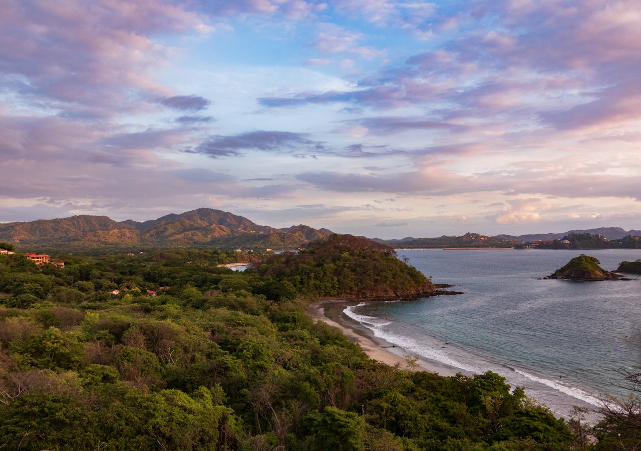 aerial view of the Guanacaste coastline at sunset with lush greenery and gentle waves.