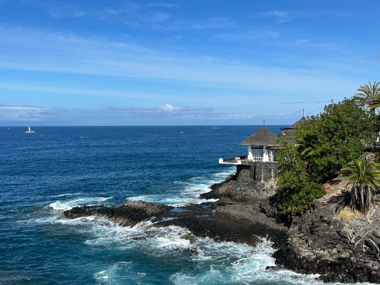 Beautiful coastline with waves crashing on rocks under a clear blue sky in Costa Adeje, Spain.